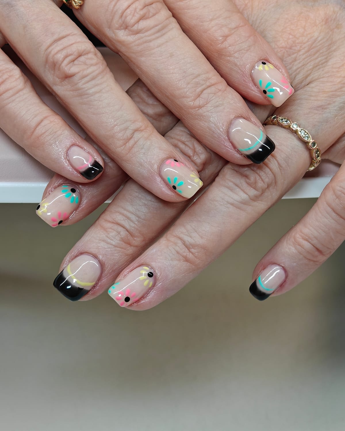 Short square nails with black and mint French tips over a nude base, scattered with pastel confetti flecks and gold specks.