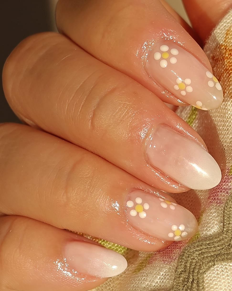 Long almond nails in a milky nude with hand-painted white and yellow daisies dotted across two accent nails.