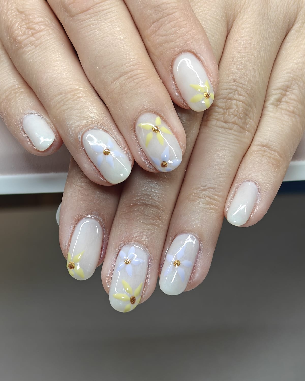 Long oval nails in milky white and sheer nude with gold caviar beads and tiny hand-painted daisies, hands crossed.