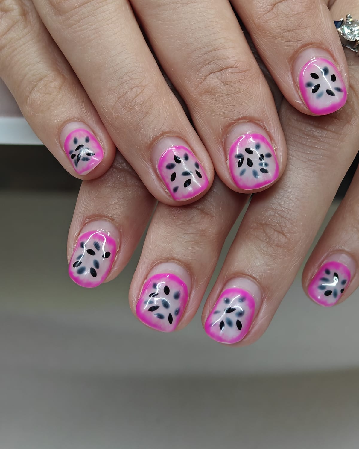 Short nails with hot pink French tips over a white base, speckled with painted black seeds in a dragon fruit pattern.