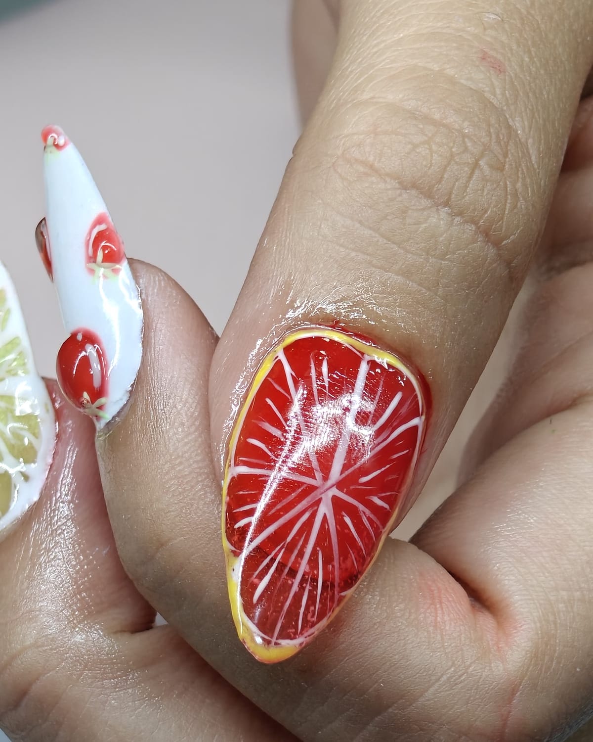 Nail work from Only Nails Beauty — macro detail of an almond nail painted as a ruby grapefruit slice beside sculpted 3D cherries.