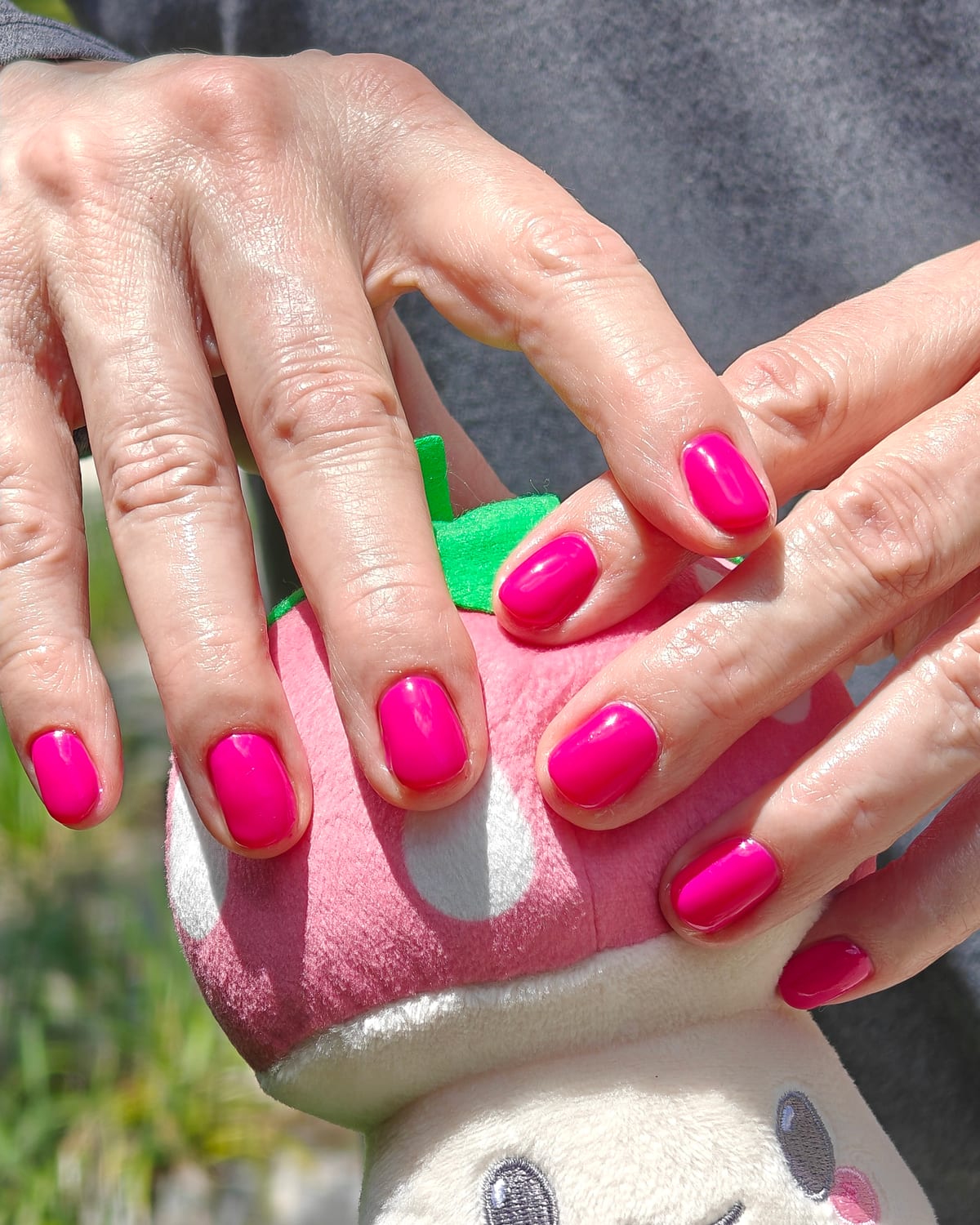 Short square nails in vivid fuchsia with a glossy finish, hands cupped around a pink and white plush toadstool.