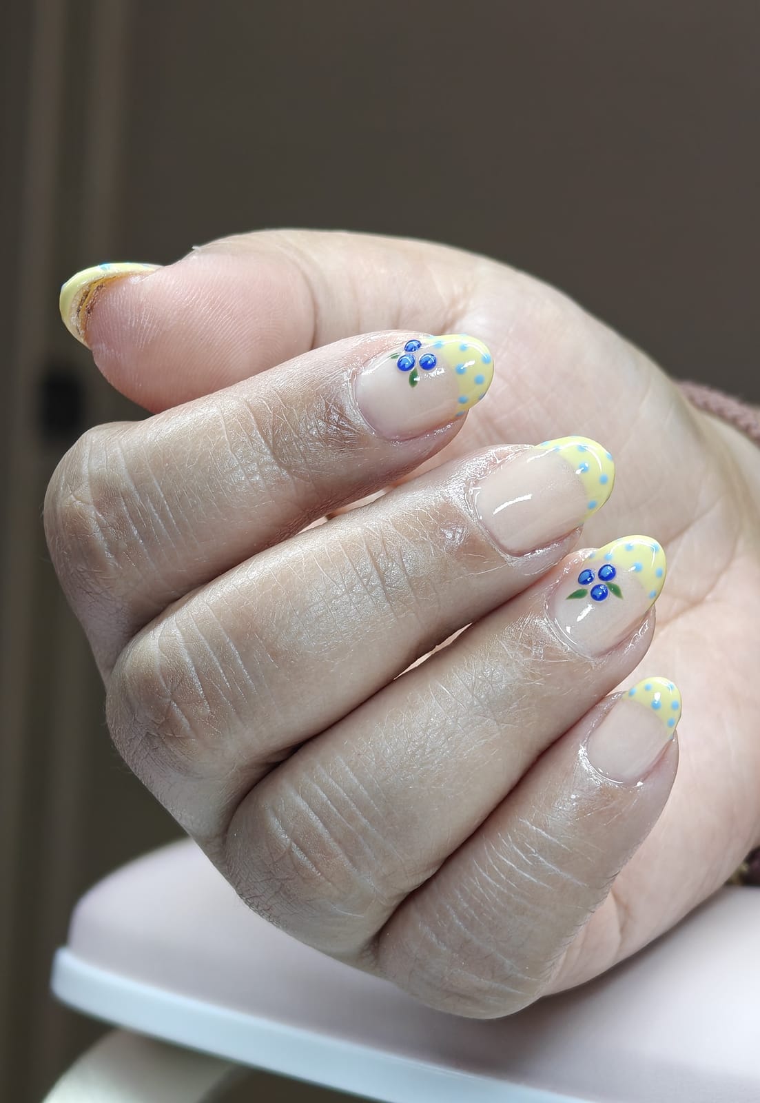 Short nails with pale yellow tips over a sheer base, finished with tiny hand-painted blue flowers and yellow dot clusters.