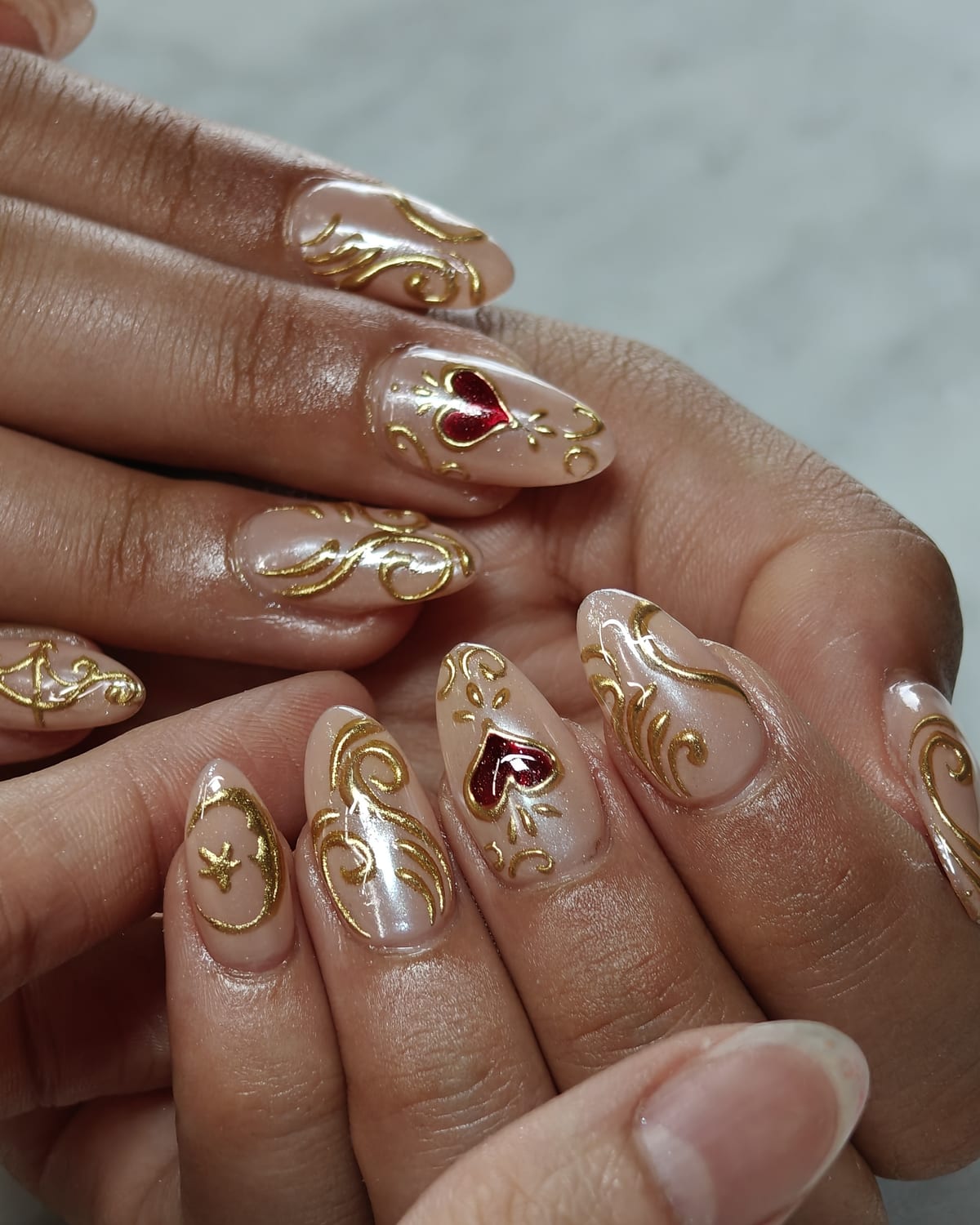 Long almond nails in pearl white with ornate gold baroque scrollwork and deep red gemstone accents hand-painted on each tip.