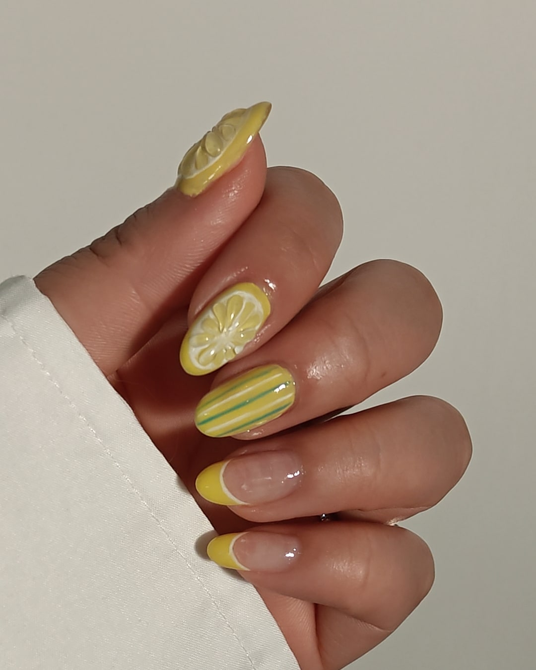 Almond nails in lemon yellow with painted stripes, a sheer citrus-slice tip and a sculpted 3D lemon wedge on the accent nail.