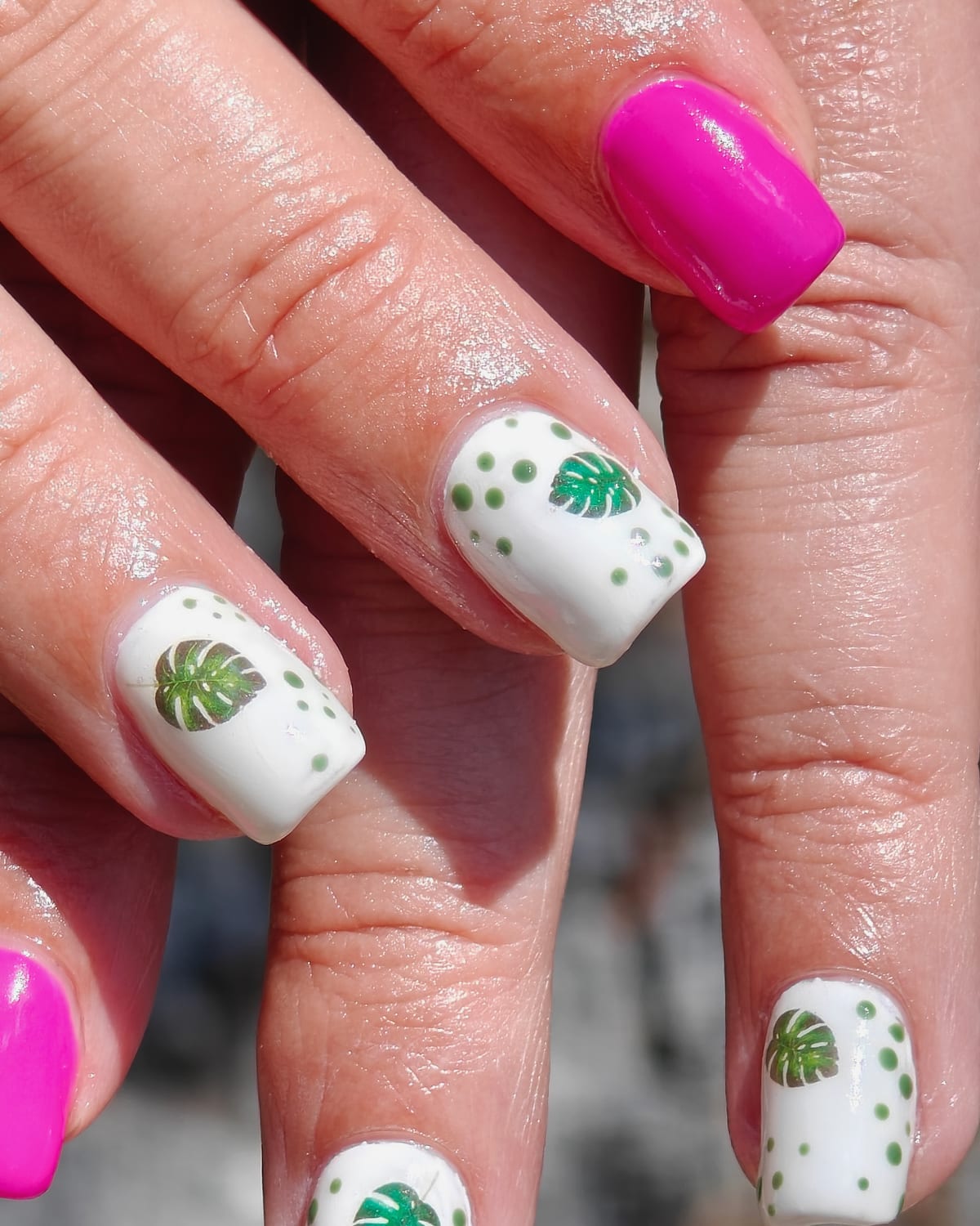 Square nails in glossy white painted with green monstera leaves and dot borders, alongside a bright magenta accent nail.