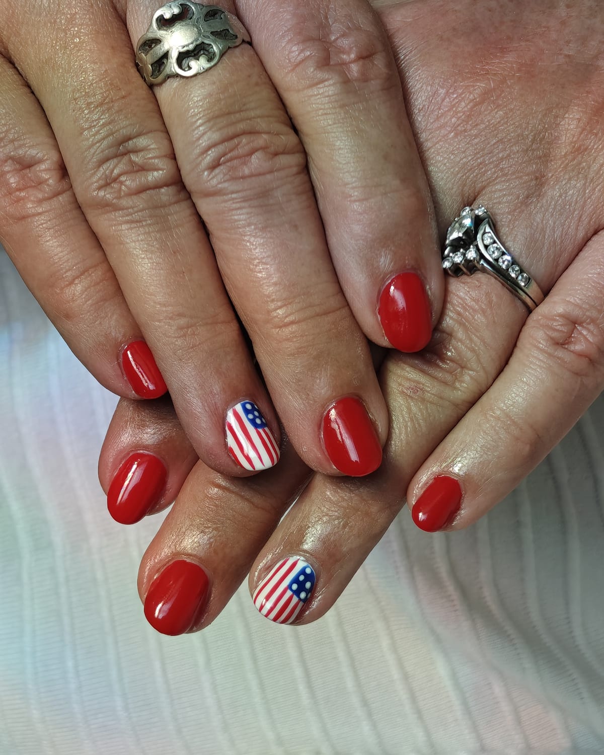 Short nails in glossy red with two accent nails hand-painted as American flags, stars and stripes, hands crossed.