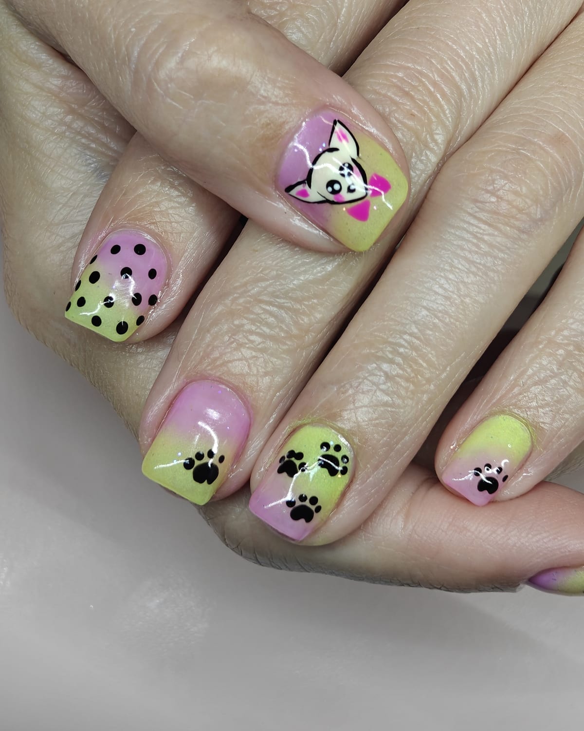 Short nails in pistachio green and lilac with black paw prints, dalmatian spots and a hand-painted cartoon cat accent nail.