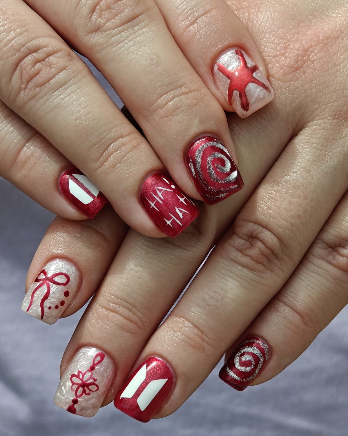 Ten square nails in cherry red and pearl white with hand-painted bows, ribbons, swirls and a starfish accent.