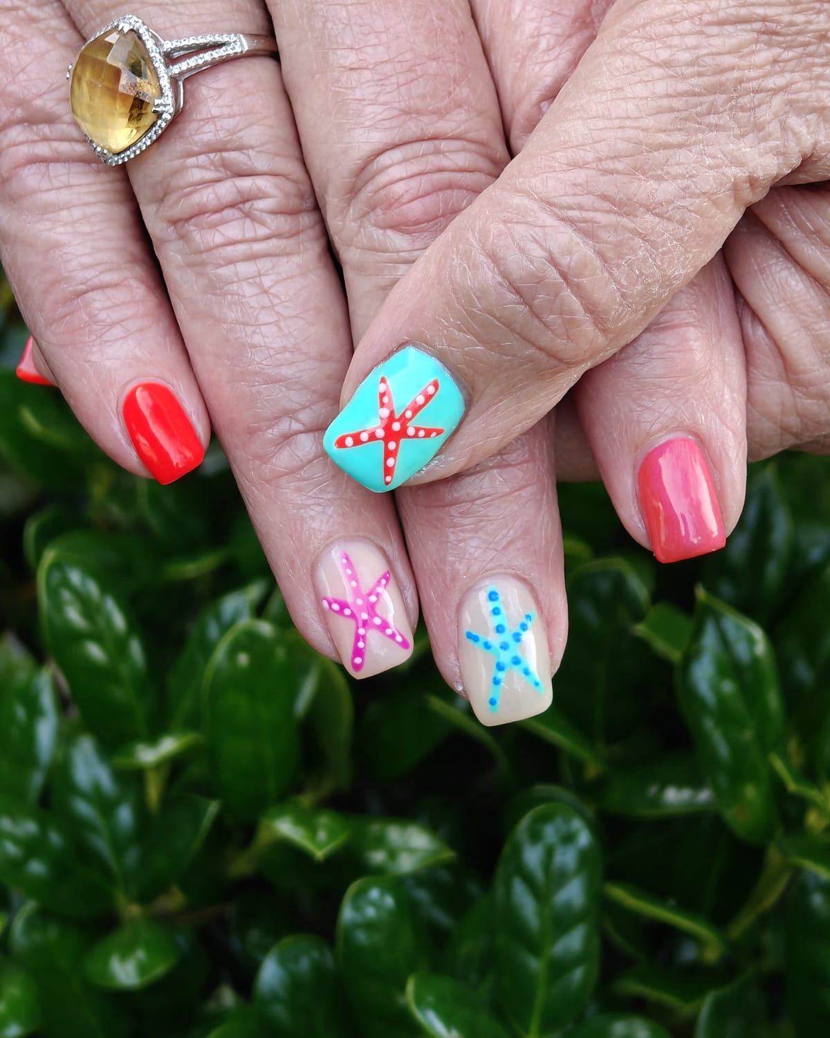Nail work from Only Nails Beauty — short square nails in coral red and turquoise with hand-painted dotted starfish accents.