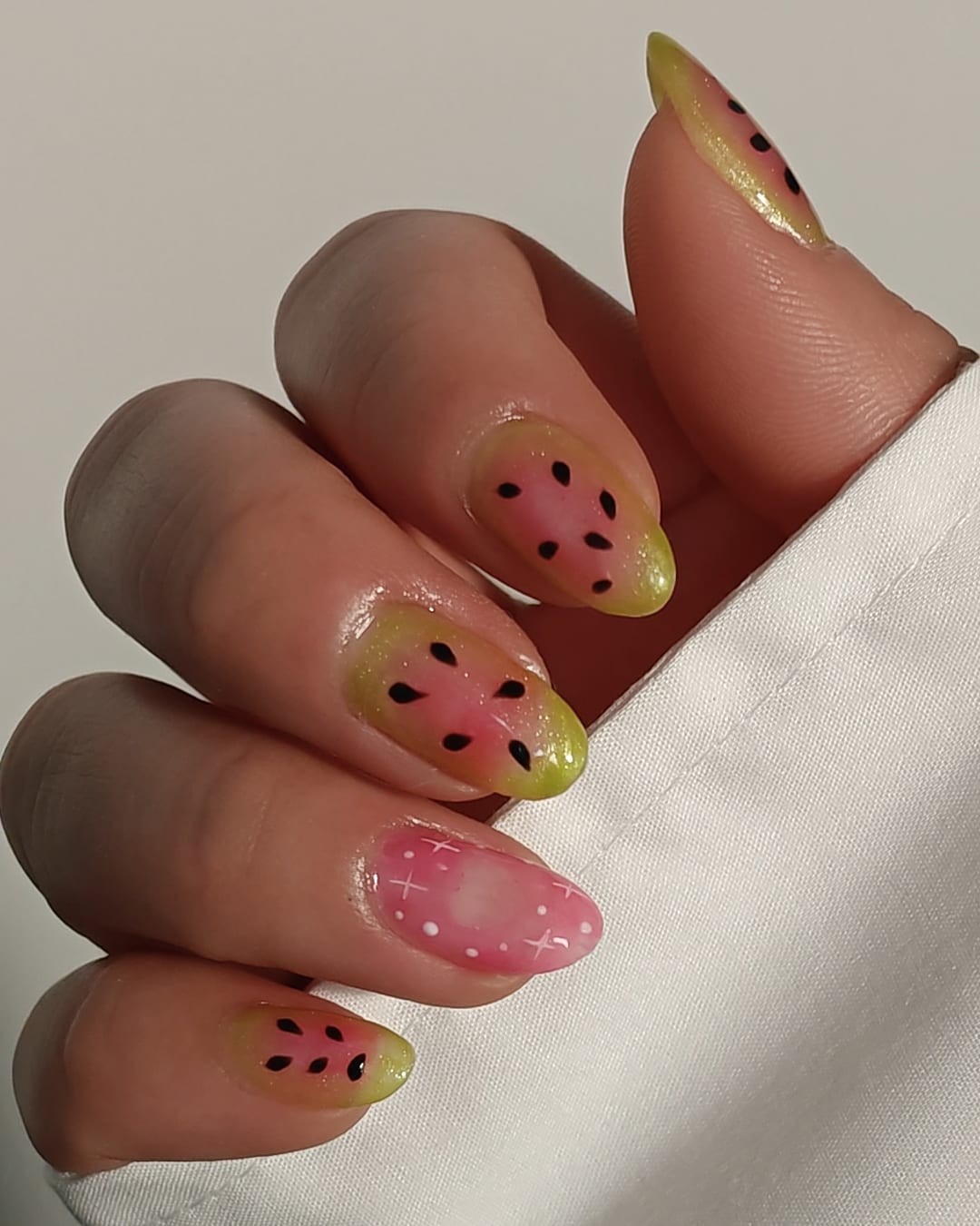 Almond nails airbrushed in watermelon pink and lime green with hand-painted black seeds and a sheer polka-dot accent nail.