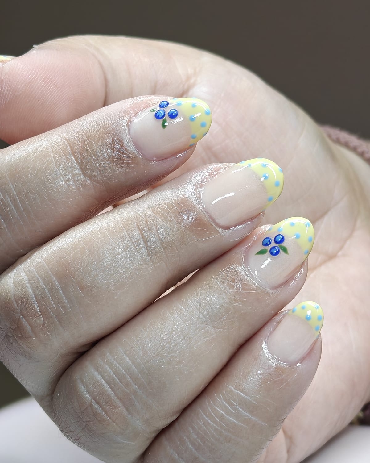 Short nails with pale yellow tips over a sheer base, finished with tiny hand-painted blue flowers and yellow dot clusters.